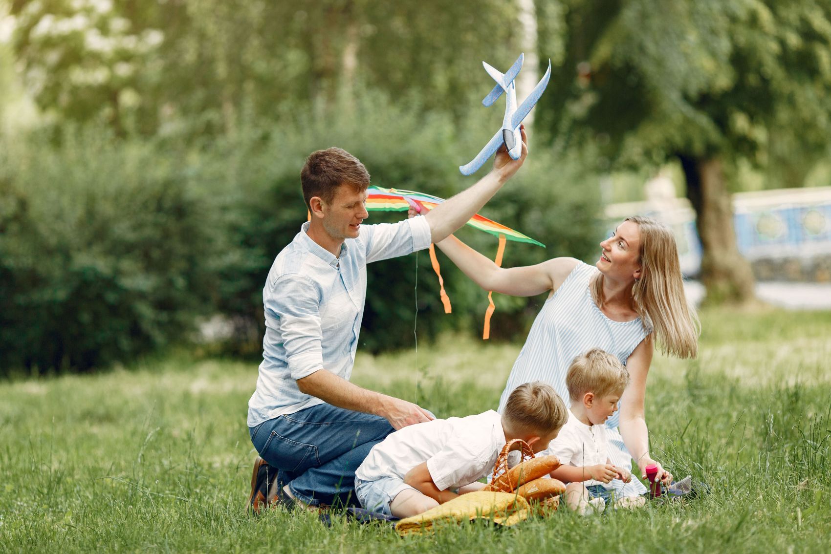 Vater, Mutter und zwei Kinder sitzen draußen im Gras und spielen mit einem Spielzeugflugzeug.
