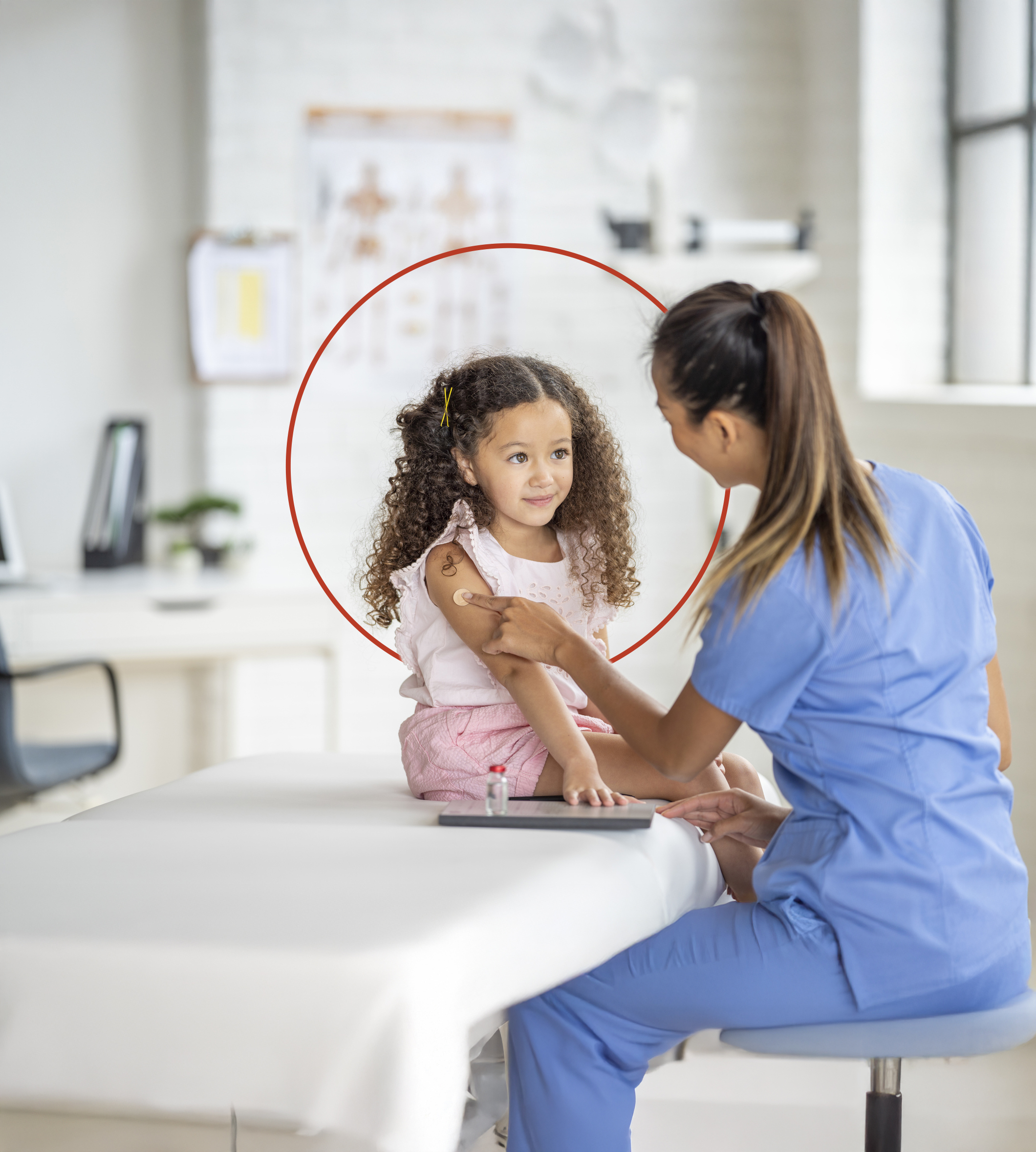 A sweet little girl of Latin decent, sits up straight on an exam table as her nurse places a bandage on her arm after giving her a vaccination. The nurse is wearing blue scrubs and smiling at the young girl to put her at ease.